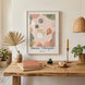Affiche « Vision & Philosophie » de Tricia Brière encadrée en bois blanc, accrochée au-dessus d'un bureau rustique en bois massif avec carnets terracotta, stylo doré, encrier vert et bougeoir laiton, dans un intérieur bohème chaleureux.