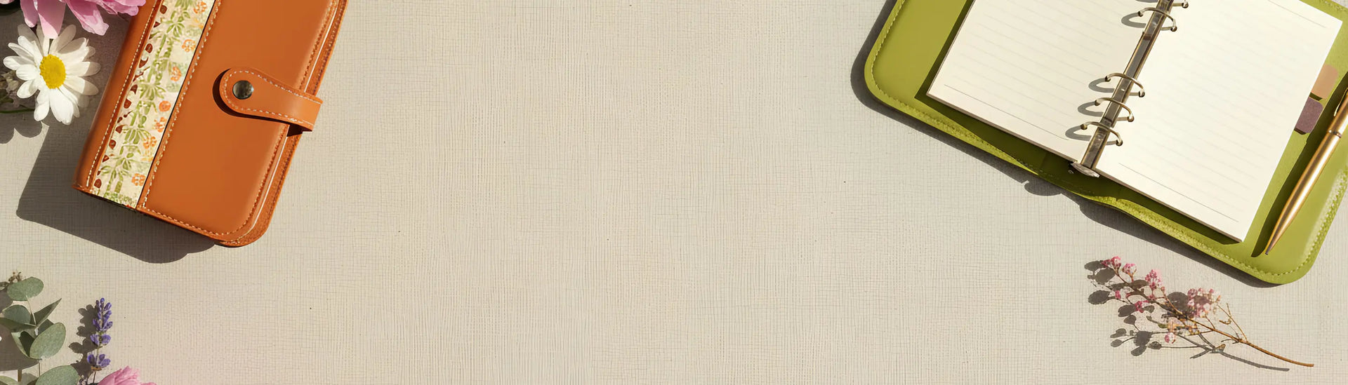 Une bannière au format paysage mettant en scène deux modèles d'organisateurs modulaires ouverts au centre de la composition, disposés sur une toile de fond beige texturée. À droite, un modèle vert pomme est ouvert, laissant entrevoir ses anneaux métalliques et ses intercalaires. À gauche, un modèle de couleur orange brulé est grand ouvert. Les deux objets sont généreusement entourés d'une composition estivale et poétique de fleurs fraîches et séchées.