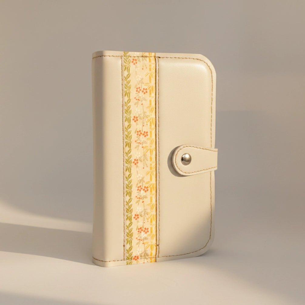 Vue de face d'un organisateur modulaire en cuir blanc cassé fermé, posé à la verticale. La lumière naturelle sculpte ses formes et met en valeur la bande centrale à motifs, la boucle de fermeture et l'élégance minimaliste de son design.