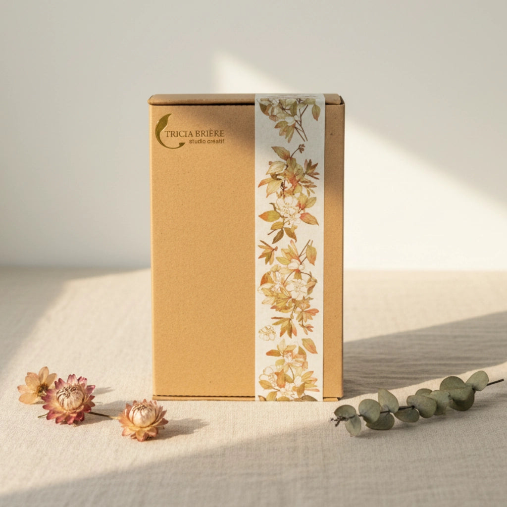 Boîte cadeau kraft Tricia Brière Studio Créatif avec bande florale botanique, mise en scène avec fleurs séchées et eucalyptus sur lin, lumière matinale — emballage papeterie et maroquinerie premium, Canada