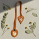 Marque-page en cuir cognac à découpe feuille et médaillon, ornés de tissus japonais fleuris et de cabochons colorés, entourés de fleurs séchées et feuilles d'eucalyptus sur fond lin naturel.
